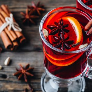 Mulled red wine with spices and orange in glass on a wooden rustic background. Homemade Christmas drink.